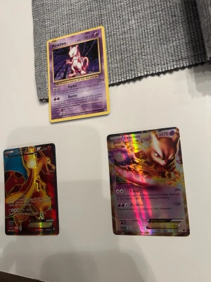 Pokémonkort Mewtwo & Charizard - Tre Pokémonkort säljes: två med Mewtwo och ett med Charizard. Ett Mewtwo-kort är klassiskt med gul ram och lila bakgrund, de andra två är holografiska med färgstarka motiv. Perfekt för samlare eller Pokémonfans.