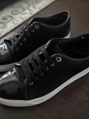 Svarta sneakers med lackdetaljer - Snygga svarta sneakers med vit sula och coola lackdetaljer på tån. Skorna har svarta skosnören och metallöljetter, vilket ger en stilren och modern look. Perfekta för dig som vill ha något klassiskt men ändå med en twist. Pris kan diskuteras!!