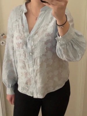 Ljusblå transparent blus med blommönster - Snygg ljusblå blus. Blusen har v-ringning, är tun och luftig. Kommer ej till användning💕