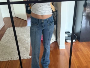 Blå bootcut jeans med låg midja - Säljer ett par blå bootcut jeans med låg midja och snygga detaljer vid fickorna. Jeansen är lite slitna här och där, det kah visar på bilderna är slitaget. Det är storlek 34