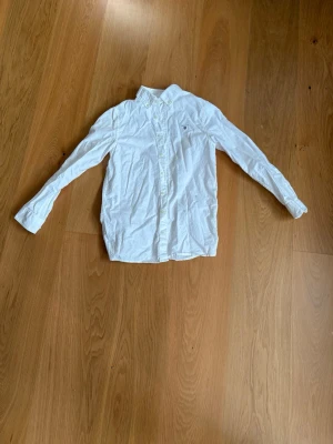 Vit skjorta från Gant med broderad logga - Klassisk vit skjorta från Gant med broderad logga på bröstet. Skjortan har lång ärm, knappar framtill och krage. Tillverkad i bomull och passar perfekt till en stilren look.