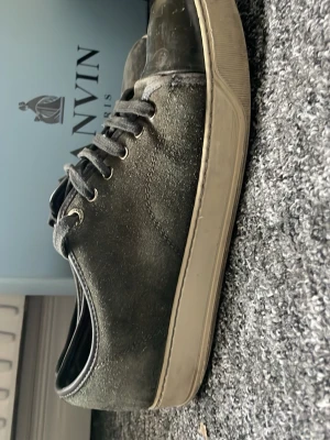 Svarta Lanvin sneakers i läder - Svarta sneakers från Lanvin med ovandel i läder och klassisk låg siluett. Skorna har svarta skosnören, metallöljetter och en vit, robust gummisula med Lanvin-logga undertill. Perfekta för en clean och stilren look.