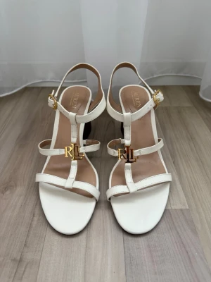 Ralph Lauren klackar - Helt oanvända!   Helt magiska klackskor från Lauren Ralph Lauren i vitt läder med vackra gulddetaljer.  En otroligt elegant sko som aldrig använts då de tyvärr inte passade, så jag hoppas att de hittar hem till någon de passar 🤍