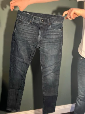Mörkblå slim fit jeans - Säljer ett par mörkblå slim fit jeans med klassisk femficksdesign och knappgylf. Jeansen har en lätt tvättad look och raka ben. Perfekta till en avslappnad stil och tillverkade i stretchig denim för extra komfort.