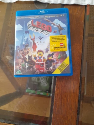 The LEGO Movie Blu-ray film - The LEGO Movie Blu-ray med färgglatt omslag som visar flera LEGO-figurer. Fodralet är blått och gjort av plast. På framsidan finns en gul etikett om Legoland-biljett. Perfekt för dig som gillar animerade filmer och LEGO.