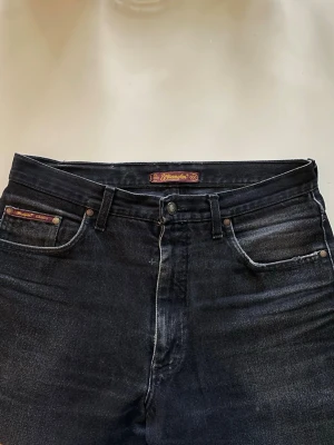 Vintage Wrangler svarta jeans  - Snygga svarta jeans från Wrangler med klassisk femficksdesign och hög midja. Jeansen har en lätt tvättad look och raka ben. Tillverkade i slitstark denim med detaljer som nitar och läderpatch bak i midjan. 