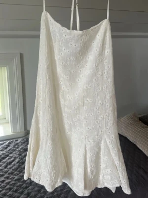 Vit somrig klänning med broderier från Zara - Superfin vit klänning med tunna axelband och broderade blommor. Klänningen har en lätt utsvängd form och är ärmlös med korsade band i ryggen. Perfekt för varma dagar, och går att både klä upp och klä ner!