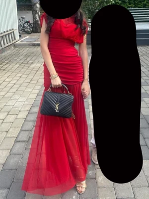 Röd långklänning med meshkjol - Snygg röd långklänning med figurnära överdel och draperad topp. Kjolen är i ett tunt meshmaterial som ger en luftig känsla. Klänningen har ärmlös design och markerad midja, perfekt för speciella tillfällen.