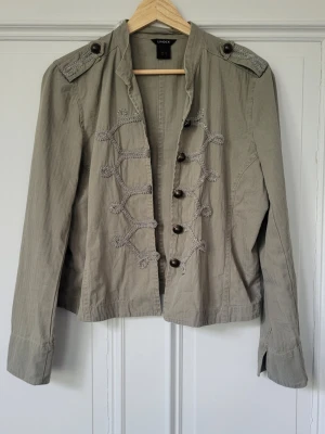 Grön militärinspirerad jacka från Lindex - Snygg militärinspirerad jacka från Lindex i ljusgrön bomull med dekorativa knappar och broderade detaljer framtill. Jackan har axelklaffar och lång ärm, perfekt för att lyfta din outfit med en cool touch. Så fin och trendig men passade tyvärr inte på mig! Storlek 44 men sitter bra på mig sobrukar ha xs/s (34-36) med? Älskar färgen!!🩷🩷