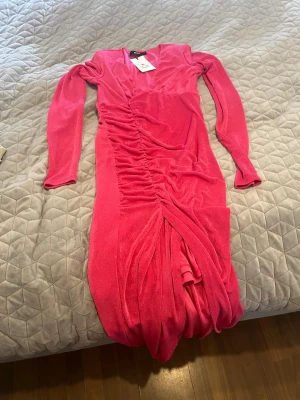 Rosa långklänning från BikBok - Snygg rosa långklänning från BikBok med långa ärmar och draperad effekt längs framsidan. Klänningen har en figurnära passform och är tillverkad i ett mjukt, stretchigt material som ger en bekväm känsla. Perfekt för dig som vill sticka ut med färg och stil.
