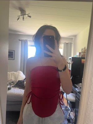 Röd bandeau tubtopp med snörning - röd bandeau tubtopp med snörning i sidorna. Toppen är axelbandslös och har en tight passform.