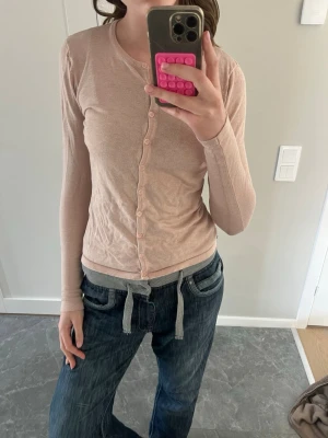Ljusrosa tunn kofta med knappar - Ljusrosa kofta med långa ärmar och rund hals, tillverkad i ett tunt och mjukt material. Koftan har små matchande knappar framtill och en enkel, stilren design som passar perfekt till jeans eller kjol. Det har funnits ett litet hål som jag har syttigen på tröjan.