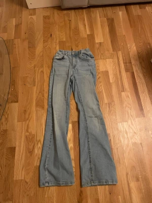 Ljusblå bootcut jeans med hög midja - Säljer ett par ljusblå bootcut jeans med hög midja och klassiska fem fickor. Ett litet hål i ena knät, och slitet på toppen av bakfickorna. Dem är lite ljusare i verkligheten och har en justerbar midja. Skickar helst med PostNord😄