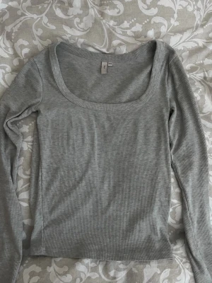 Ljusgrå ribbad långärmad topp - Säljer en ljusgrå ribbad långärmad topp. Toppen har en bred, fyrkantig urringning och är tillverkad i mjukt, stretchigt material som sitter snyggt på kroppen. 