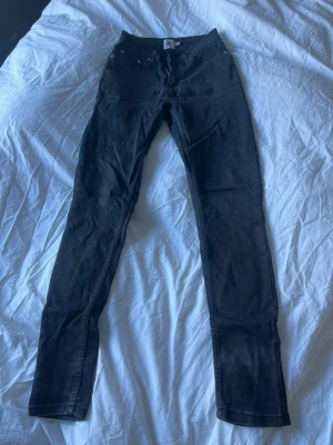 Svarta skinny jeans med hög midja - Säljer ett par svarta skinny jeans med hög midja och klassisk femficksdesign. Jeansen har smal passform hela vägen ner och är tillverkade i stretchigt denimtyg för extra komfort. 