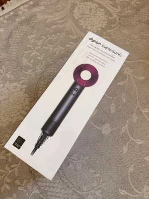 Dyson Supersonic hårfön OANVÄND O ÖPPNAD  - Dyson Supersonic hårfön i svart och lila med innovativ design och flera munstycken för olika stylingbehov. Levereras i originalförpackning och är tillverkad i plast och metall. Perfekt för dig som vill ha en kraftfull och modern hårfön.
