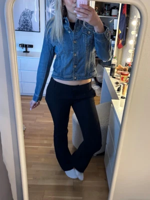 Klassisk blå jeansjacka - Snygg blå jeansjacka med figurnära passform och klassiska detaljer som bröstfickor med lock och knappar framtill. Jackan har långa ärmar och markerade sömmar som ger en tidlös look. Perfekt att slänga över en t-shirt för en cool vardagsstil.
