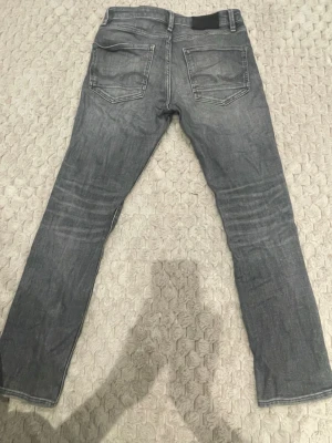 Grå slim fit jeans - Säljer ett par grå slim fit jeans med klassisk femficksdesign och snygga slitningar. Jeansen har raka ben och normal midja. Perfekta för en avslappnad och trendig look. Materialet är mjukt denim i bomull. Sen är det en liten fläck som syns lite men inte alls mycket.