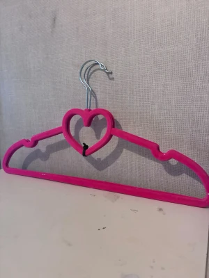 2st rosa galgar med hjärtdetalj - Säljer 2st söta galgar i stark rosa färg med en hjärtformad detalj i mitten. Galgarna har en metallkrok och är klädd i ett sammetsliknande material som gör att kläderna inte glider av. Perfekt för att hänga upp favoritplaggen på ett fint sätt.