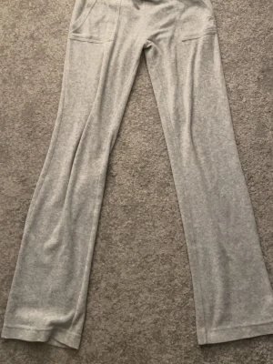 Grå mjukisbyxor med raka ben - Snygga grå mjukisbyxor från juicy couture, med raka ben och dragsko i midjan. Byxorna har fickor framtill och är gjorda i ett mjukt och bekvämt material, perfekt för en avslappnad stil. Passar dig som gillar enkel och stilren design. Har tappat sina metall grejer på snörena och har lite slitage på benet men inget man tänker på 