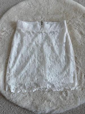 Vit spetskjol från Gina Tricot - Säljer en vit kortkjol från Gina Tricot i storlek XS. Kjolen har ett vackert spetsmaterial med fina detaljer och en dragkedja bak. Perfekt för dig som gillar en feminin och stilren look.