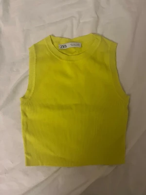 topp från Zara - Säljer en croppad ärmlös topp från Zara i en neongul färg. Toppen är ribbad och har en rund halsringning med tight passform. Perfekt för neon tema! Passar även en xs!❤️❤️