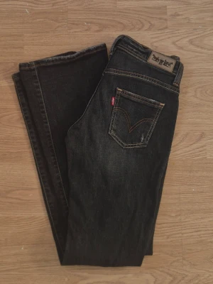 Svarta bootcut jeans från Levi's - Snygga svarta bootcut jeans från Levi's med klassiska fem fickor och kontrastsömmar. Jeansen har en mörk tvätt och den röda Levi's-taggen på bakfickan. Perfekta för en trendig och avslappnad stil.