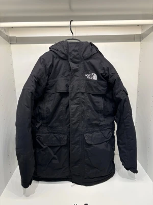 The North Face jacka  - Säljer en svart jacka från The North Face med huva och flera praktiska fickor framtill. Jackan har en klassisk logga på bröstet och ryggen, dragkedja och vindslå. Perfekt för kalla dagar och riktigt snygg streetstil. Materialet är slitstarkt och vattenavvisande.