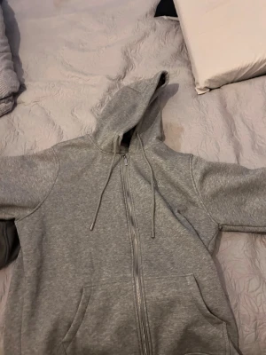 Burberry hoodie  - Säljer en grå hoodie med dragkedja och fickor framtill. Huvan har ett klassiskt rutigt mönster på insidan i beige, svart och rött. Utsidan är enkel och stilren medan insidan är mjuk och vit. Perfekt för dig som gillar en chill och snygg stil.