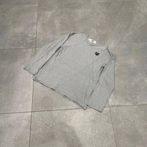 CDG longsleeve - Är storlek L men sitter som S själv har jag S och den passar perfekt. Snygg grå långärmad t-shirt från Comme des Garçons Play med det ikoniska hjärte-logotypen på bröstet. Tillverkad i mjuk bomull och har en klassisk passform som funkar till allt. Perfekt för dig som gillar stilrena och trendiga plagg.