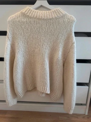 Krämvit chunky stickad tröja - Mysig chunky stickad tröja i krämvit färg med bred ribbad polokrage och långa ärmar. Oversized passform och grovstickat material som ger en avslappnad look. Perfekt för lager på lager under kalla dagar.