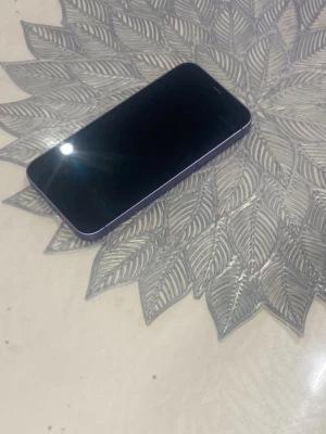 Lila iPhone 12 med dubbla kameror - Säljer en snygg lila iPhone 12 från Apple. Telefonen har en stilren design med platt glasfront och baksida, samt aluminiumram. Baksidan har två kameror och den klassiska Apple-loggan. Perfekt för dig som vill ha en modern och färgglad mobil. Den funkar jätte bra och pris kan diskuteras 