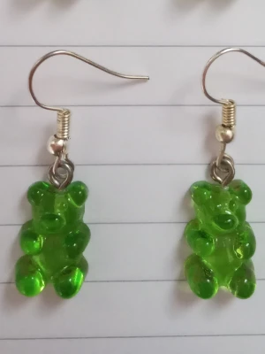 Gröna björn örhängen  - Säljer ett par unika örhängen med gröna gummibjörns-hängen i plast. Örhängena har krokar i metall och är knappt använda. 