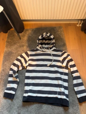 Randig hoodie med marinblå och vita ränder - Snygg hoodie med breda marinblå och vita horisontella ränder. Tröjan har huva med dragsko och muddar vid ärmslut och nederkant. Perfekt för en avslappnad och cool stil. Materialet känns mjukt och bekvämt mot huden.