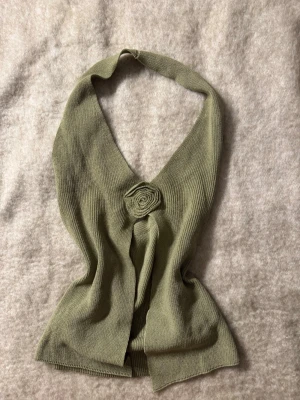 Ljusgrön stickad halterneck topp - Trendig ljusgrön stickad halterneck topp med v-ringning och dekorativ virkad blomma framtill. Toppen har en croppad passform och är perfekt för dig som vill ha en unik och stilren look.