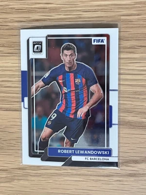 Fotbollskort Robert Lewandowski - Säljer ett samlarkort från Panini Donruss Optic med Robert Lewandowski i FC Barcelona. Kortet har en färgstark design med klubbens blå och röda ränder och Lewandowskis namn tryckt på framsidan. Perfekt för dig som gillar fotboll och samlar på sportkort.