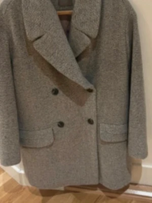 Grå ullkappa med bred krage  helt ny  - Stilren grå kappa i ullmix med dubbelknäppning och bred krage. Kappan har två fickor framtill och en rak, klassisk passform. Perfekt för kyliga dagar och ger en snygg siluett. köpt för 1600