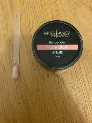 Miss Fancy Builder Gel Nude Blush - Builder gel i färgen Nude Blush från Miss Fancy Professional. Gelen har en mjuk nude-rosa ton och passar perfekt för att bygga och förstärka naglar. Används med UV eller LED-lampa. Förpackningen innehåller 50g gel.