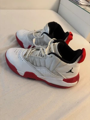 Vita och röda Air Jordan sneakers - Säljer ett par vita och röda Air Jordan sneakers med svart Jumpman-logga på sidan och röd sula. Skorna har meshdetaljer på sidorna, perforeringar framtill och signaturen samt siffran 23 på hälen. Lågt skaft och klassisk snörning. Perfekta för dig som gillar streetwear.