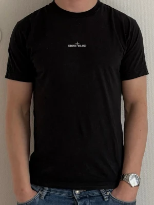 Svart Stone Island t-shirt med tryck - Stone Island t-shirt med stort backprint. Köpt på NK för några år sedan. Använt skick med mindre hål/slitage vid ena ärmen (se sista bild), därav priset. Printen fram och bak fortfarande i bra skick.
