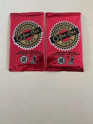 O-Pee-Chee Premier hockeykort 1993 - Två oöppnade paket O-Pee-Chee Premier hockeykort från 1993. Varje paket innehåller 7 hockeykort och 1 insert card. Förpackningarna är metallicröda med tydlig logotyp och NHL/NHLPA-märkning. Perfekt för samlare av sportkort.