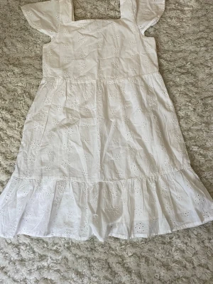 Vit broderad sommarklänning - Söt vit klänning i bomull med broderade blommor och volang nertill. Klänningen har korta ärmar och fyrkantig ringning, perfekt för varma dagar. Lätt och luftig modell som ger en romantisk känsla. Perfekt till skolavslutning eller en sommardag! Endast använd en gång.