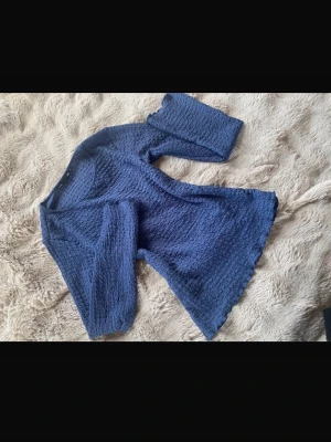Blå strukturerad långärmad tröja - Mysig blå långärmad tröja med vågig kant och strukturerat tyg. Tröjan har en rund halsringning och är tillverkad i ett stretchigt material som ger en cool textur. Perfekt för dig som gillar en avslappnad men ändå trendig stil.