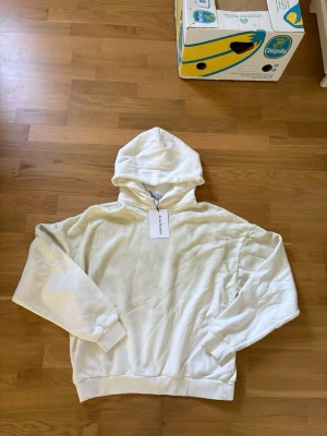 Vit hoodie från Acne Studios - Säljer en stilren vit hoodie från Acne Studios med klassisk huva och ribbade muddar. Hoodien är tillverkad i mjukt material och har en avslappnad passform. Perfekt för en clean och modern look.