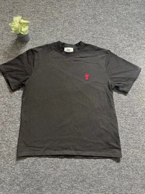 Svart t-shirt från AMI Paris - Svart t-shirt från AMI Paris med klassisk passform och korta ärmar. På bröstet finns ett litet rött broderat hjärta med A. Tillverkad i mjuk bomull och perfekt för en clean och stilren look.