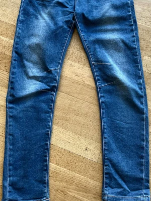 Blå jeans med slitningar - Snygga blå stretchiga jeans med diskreta slitningar på framsidan. Relaxed fit.