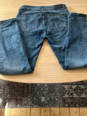 Blå slim fit jeans med fem fickor - Snygga blå slim fit jeans med klassisk femficksdesign och dragkedjegylf. Jeansen har en lätt tvättad look och raka ben. Perfekta för en avslappnad stil och passar till det mesta. Materialet är mjukt denim i bomullsblandning.