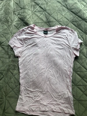 Ljusrosa t-shirt från Gina Tricot - En basic ljusrosa t-shirt från Gina Tricot i mjuk bomull. Modellen är klassisk med rund halsringning och korta ärmar. Perfekt att matcha med jeans eller kjol för en enkel och snygg look.