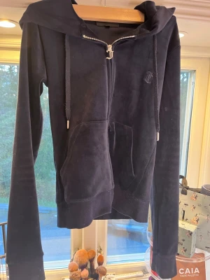 Mörkblå velour hoodie Juicy Couture - Säljer en mörkblå hoodie från Juicy Couture i mjuk velour med dragkedja och två fickor framtill. Hoodien har huva med snören och diskret logga på bröstet. Perfekt för dig som gillar en avslappnad och trendig look.