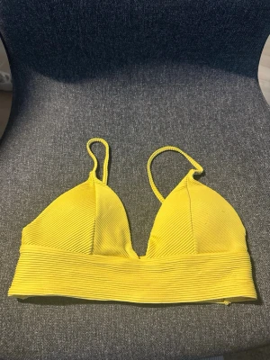 Gul ribbad bh med smala axelband - Gul bikiniöverdel med ribbad struktur och smala axelband. Modellen har en bred resår under till för extra stöd och en enkel, stilren look. Perfekt för soliga dagar vid stranden eller poolen.